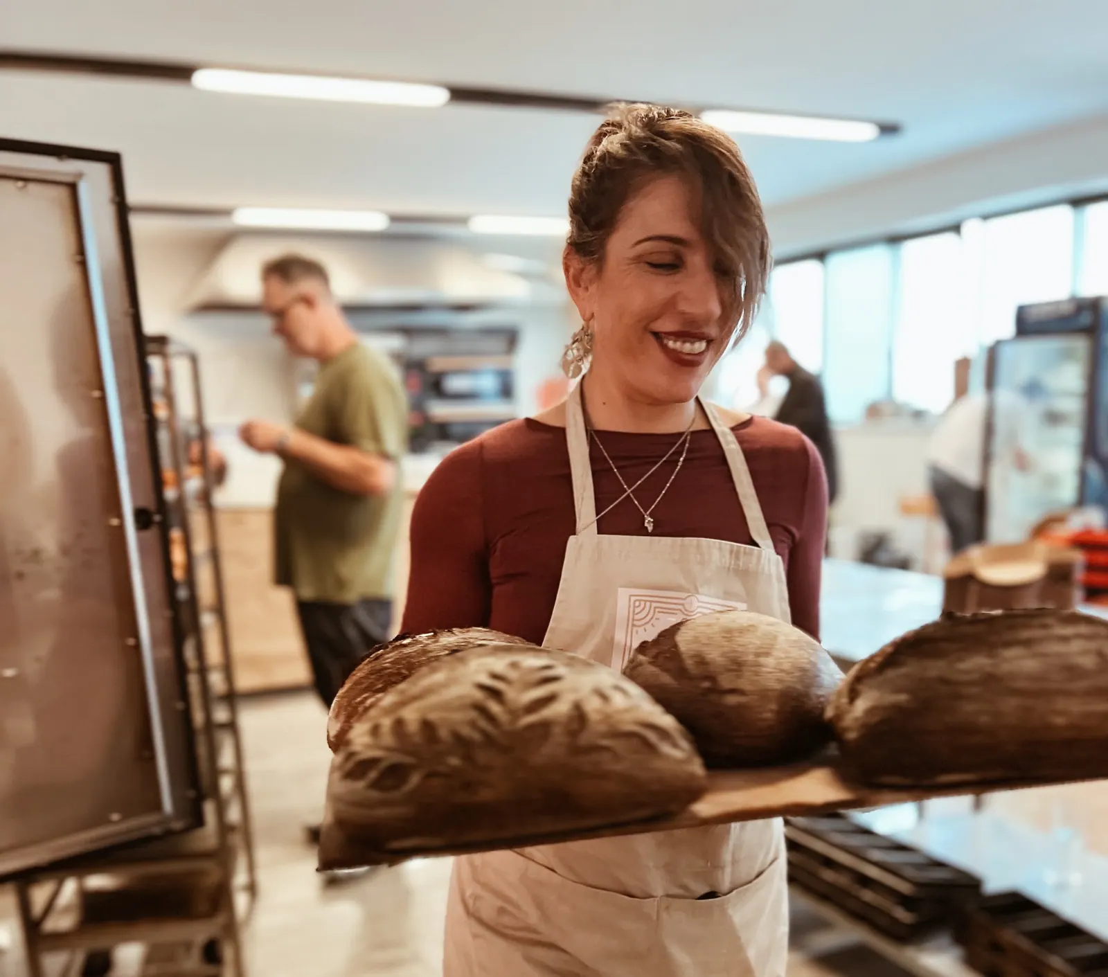 A baker smiling over a board of her dark sourdough loaves