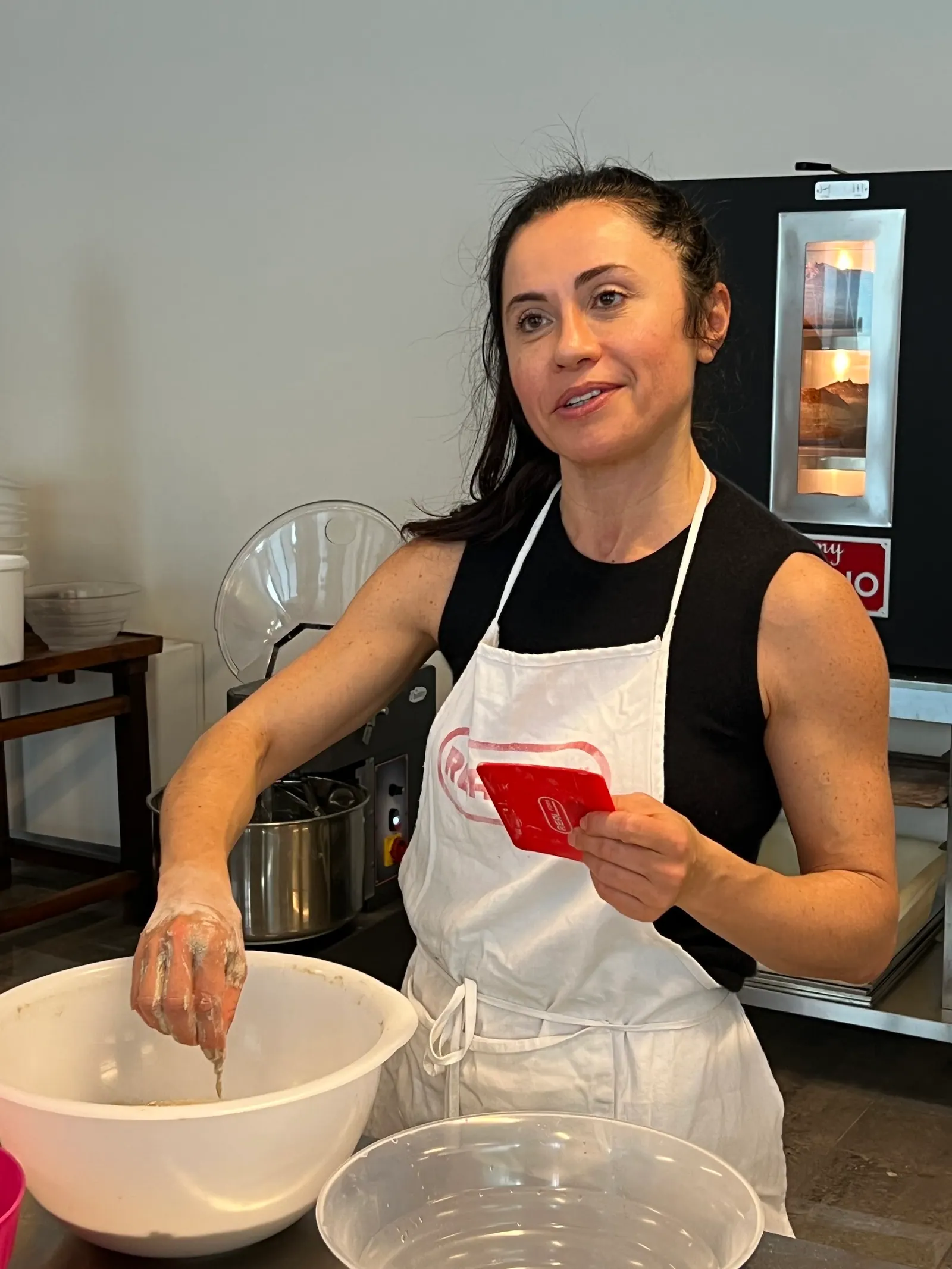 A baker mixing dough in front of a MyForno oven