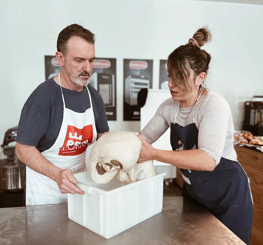 Two bakers lifting a large dough out of a white tub