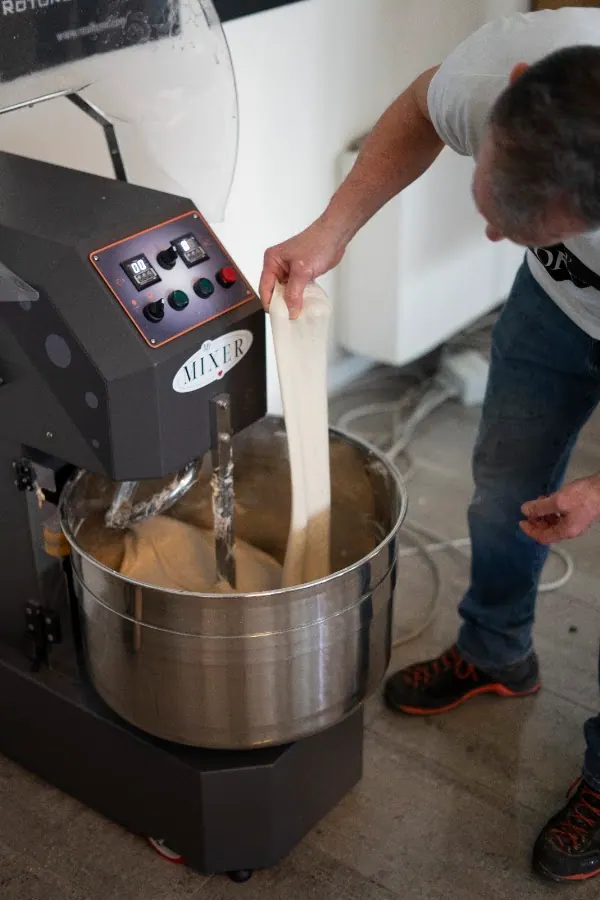 A baker lifting a long ribbon of dough from a spiral mixer