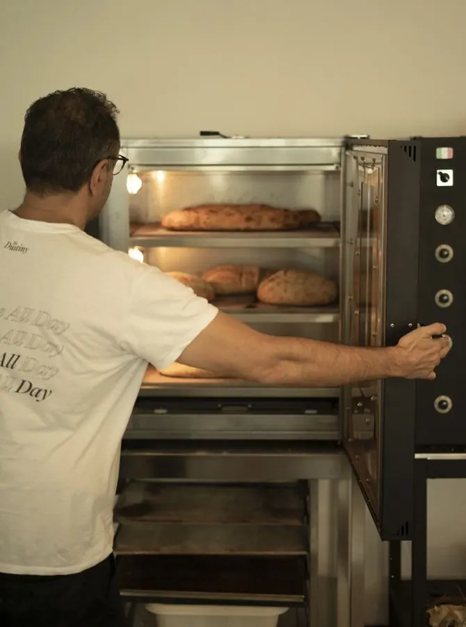 A baker checking loaves in the oven