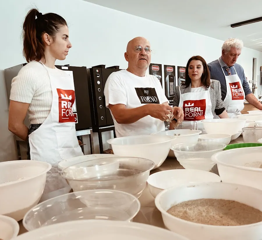Four bakers in aprons mixing dough in white bowls at a long bench