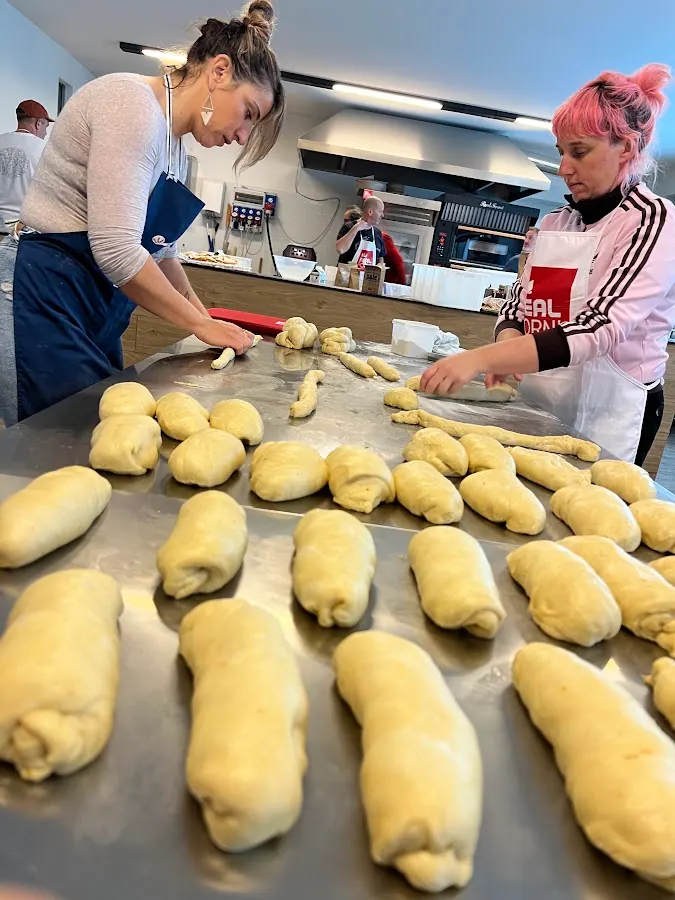 Two bakers shaping rows of rolls on a steel bench
