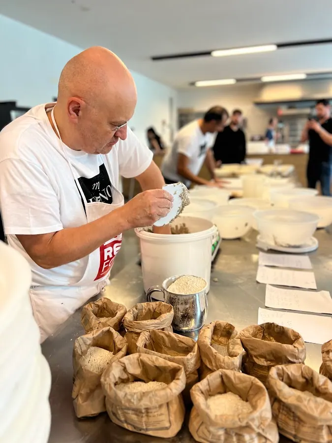 A baker weighing flour into a bowl beside paper bags of flour