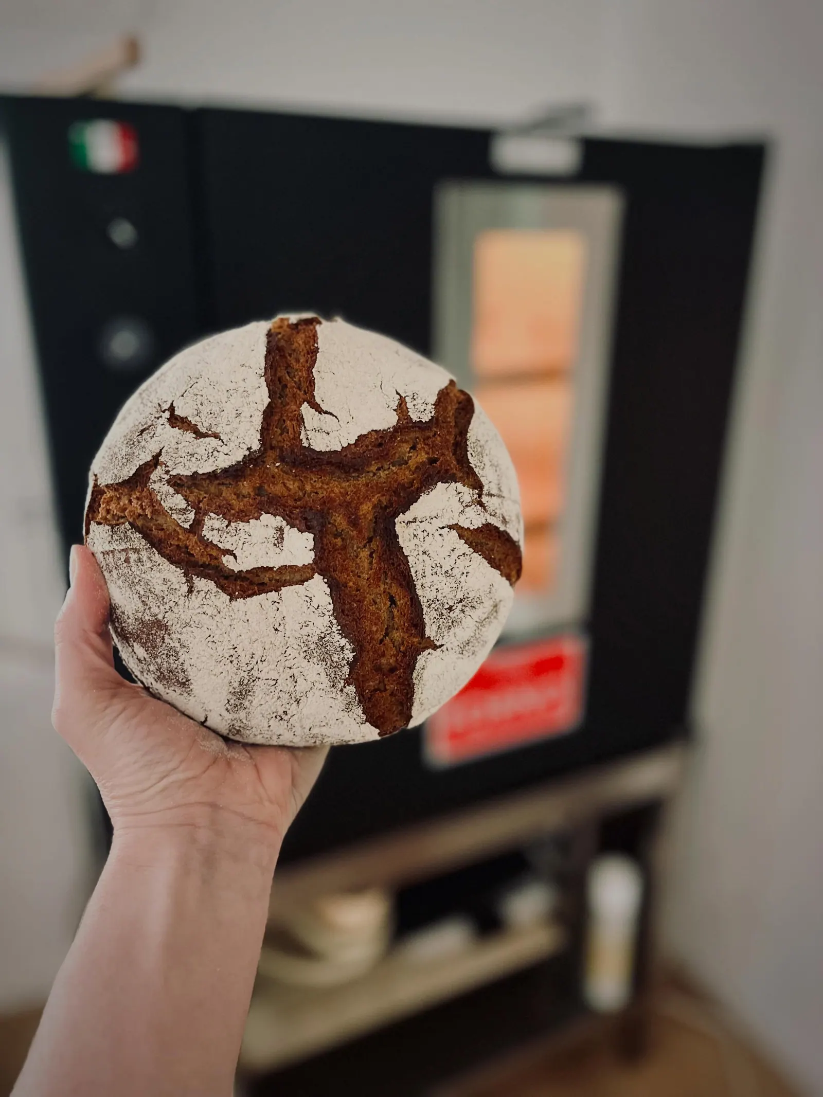 A Smittenbrot rye loaf held up beside the MyForno oven