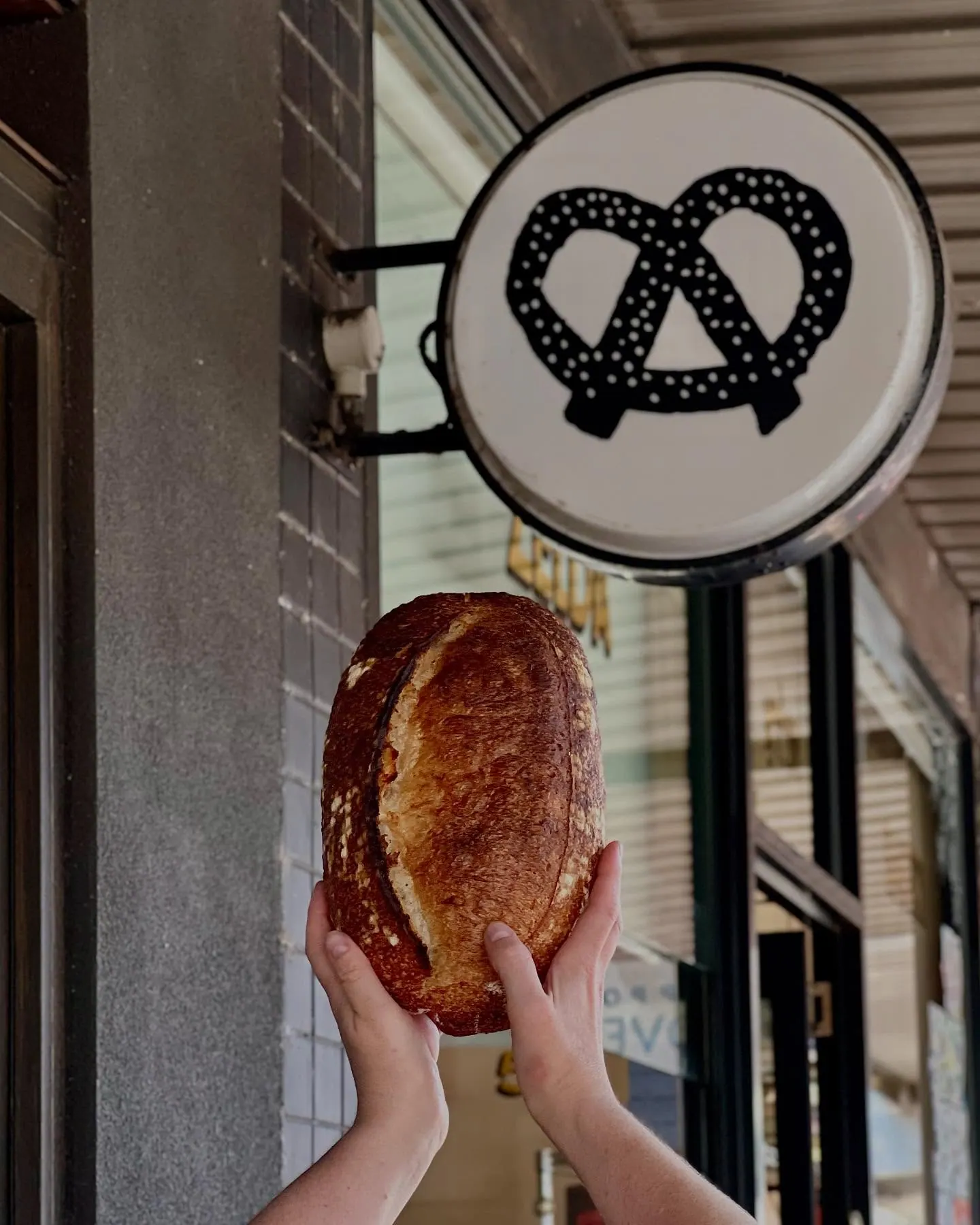 A Zelda Bakery loaf held up under the shop sign